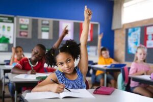 A child in a classroom raising their hand confidently, symbolizing the source of their energy is a healthy breakfast.